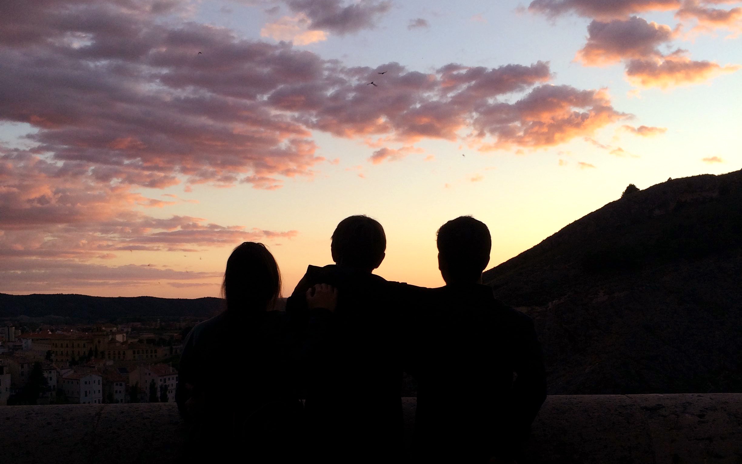 Three silhouettes standing on a balcony looking at the sunset in Cuenca, Spain.